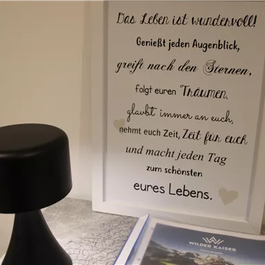 Ein stilvolles Schwarz mit einer runden Lampe und einem gerahmten Zitat über das Leben. Darunter liegt ein Prospekt mit einer schönen Landschaft.