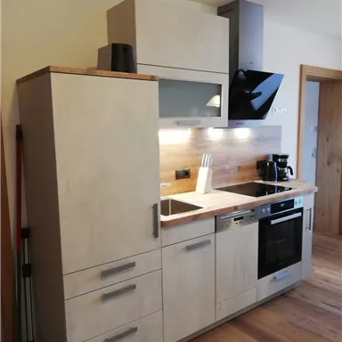 A modern kitchen with a clear, minimalist design. It features wooden and gray cabinet elements as well as modern appliances.