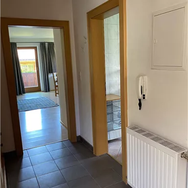Ein heller Flur mit zwei offenen Türen und Fliesenboden. Auf der rechten Seite befindet sich ein Heizkörper.