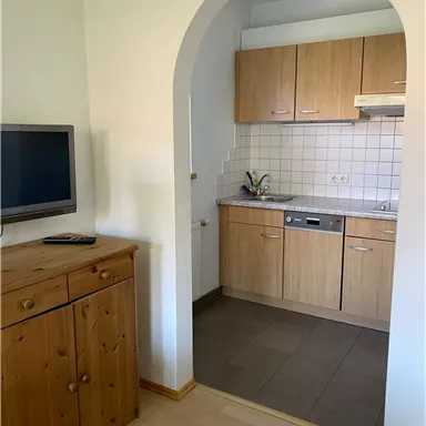 Eine moderne Küche mit Holzschränken und einem großen Kühlschrank. Der Eingang ist durch einen runden Bogen gekennzeichnet.