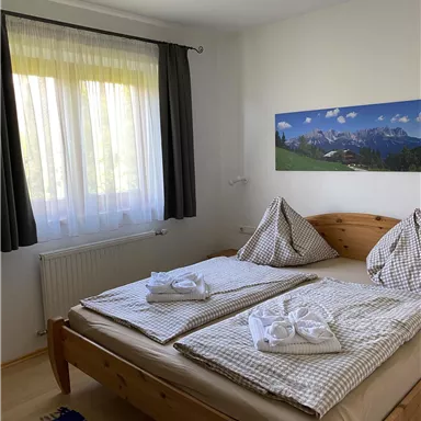 Ein helles Schlafzimmer mit zwei Einzelbetten und einem großen Fenster. Die Wände sind in neutralen Farben gehalten und ein Landschaftsbild ziert die Wand.