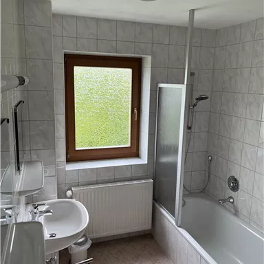 Ein modernes Badezimmer mit einer Badewanne und einer Dusche. Ein Fenster sorgt für Tageslicht und frische Luft.