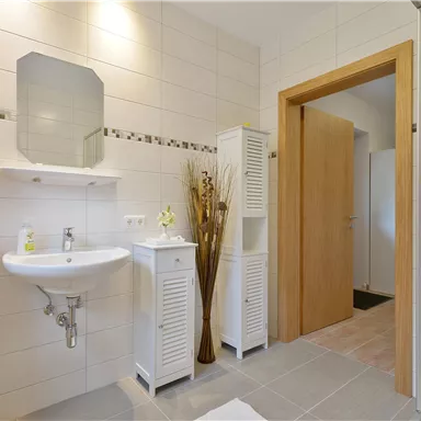 Ein modernes Badezimmer mit hellen Fliesen und einem klaren Design. Handtücher in Orange und eine große Duschnische vervollständigen den Raum.