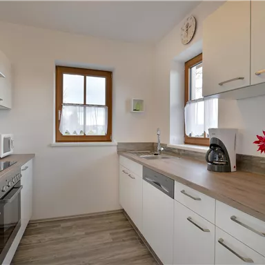 Eine moderne Küche mit weißen Möbeln und Holzdetails. Sie ist hell und einladend mit einem Fenster, das für natürliches Licht sorgt.