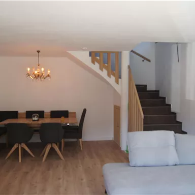 A modern living room with a comfortable couch and a dining area. A staircase leads to the upper part of the room.