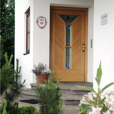 Eine gemütliche Haustür aus Holz mit einem bunten Glaselement. Im Vordergrund befinden sich Grünpflanzen und Blumen.