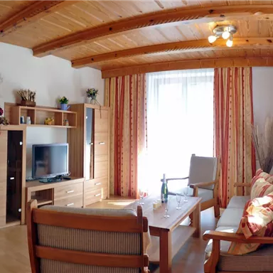 A cozy living room with wood paneling and large windows. There is a couch, a television, and a wooden table.