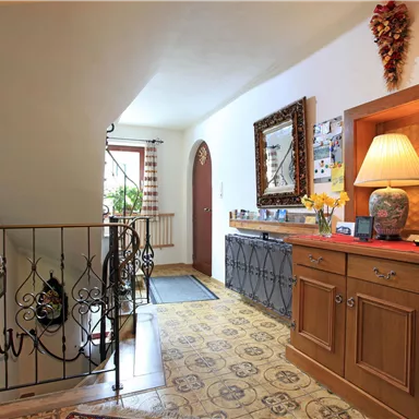 Ein einladender Flur mit einem Holzschrank und einem schönen Teppich. An der Wand hängen Bilder und eine Lampe sorgt für warmes Licht.