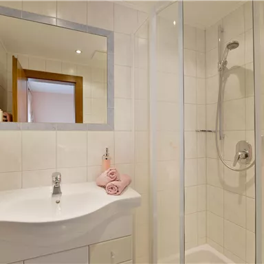 A modern bathroom with a shower and a sink. On the sink, there are pink towels.