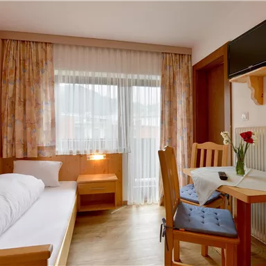 A cozy room with a single bed, a table, and chairs. Large windows provide plenty of daylight.