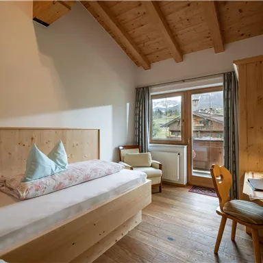 Ein gemütliches Zimmer mit Holzmöbeln und einem großen Fenster. Im Hintergrund sind die Berge sichtbar, und das Tageslicht strahlt herein.