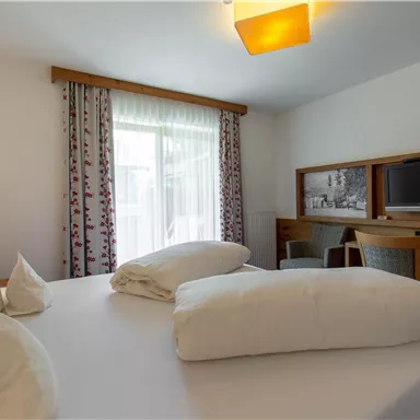 Ein gemütliches Hotelzimmer mit einem großen Bett und modernen Möbeln. Es gibt Fenster, die viel Tageslicht hereinlassen, sowie einen Fernseher und einen Arbeitsplatz.