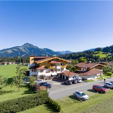 Ein malerisches Hotel in einer ländlichen Umgebung mit grünen Wiesen und Bergen im Hintergrund. Das Wetter ist schön und klar, ideal für einen Aufenthalt in der Natur.