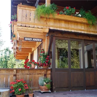 Ein traditionelles Holzhaus mit einem Balkon, der mit Blumen dekoriert ist. Der Eingangsbereich ist einladend und freundlich gestaltet.