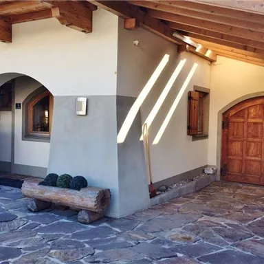 A modern house with a wooden roof and a rustic entrance door. The entrance area is decorated with cobblestones and a wooden bench.