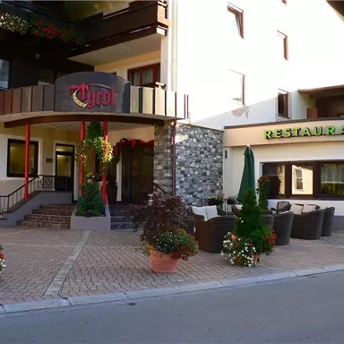 Ein einladendes Restaurant mit schön dekoriertem Außenbereich. Im Vordergrund sind Pflanzen in Töpfen und Sitzgelegenheiten zu sehen.