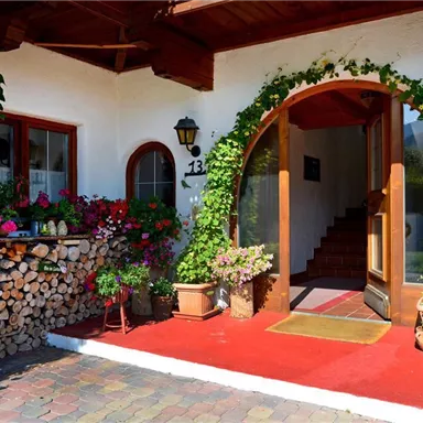 Ein einladender Eingangsbereich mit bunten Blumen und einem Holzstapel. Die Treppe und die schönen Pflanzen schaffen eine gemütliche Atmosphäre.
