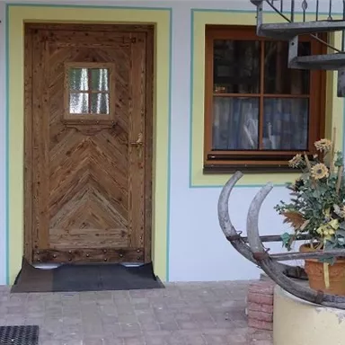 Eine rustikale Holztür mit einem schönen Muster und einem Fenster daneben. Vor der Tür steht ein Blumentopf mit bunten Blumen.