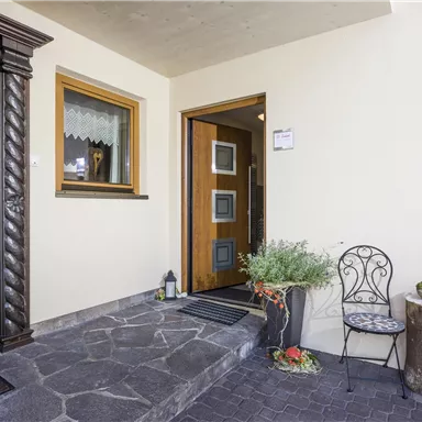 An inviting entrance area with a beautiful door and a cozy chair. Plants and a small lantern give the space a pleasant atmosphere.