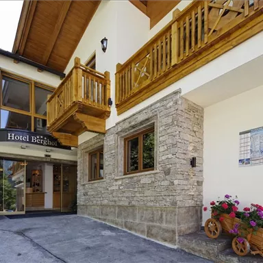 An inviting hotel with wooden cladding and a beautiful terrace.  
Flowers in a decorative container and an information card complete the picture.