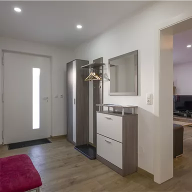 A bright hallway with a modern cabinet, a mirror, and a shoe rack. A red bench complements the elegant design.