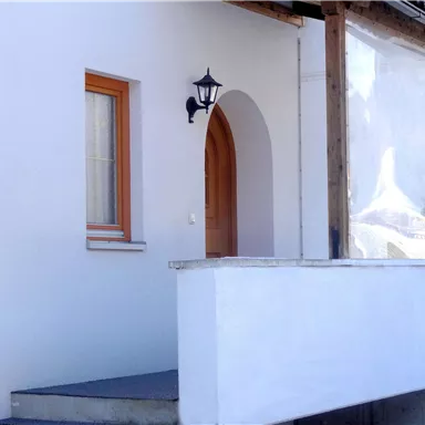 Ein modernes Haus mit einem Eingang und einer Veranda. Die Fenster haben orangefarbene Rahmen und das Umfeld ist verschneit.