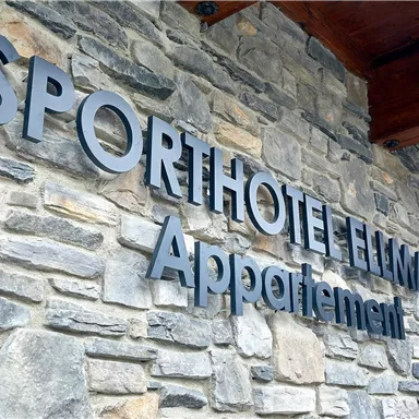 Ein sportliches Hotel mit dem Namen "Sporthotel Element" steht auf einer steinernen Wand. Darunter ist das Wort "Appartements" zu sehen.