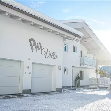 A modern, snow-covered house with the inscription "Aqua Villa". The facade is bright and inviting under a clear sky.