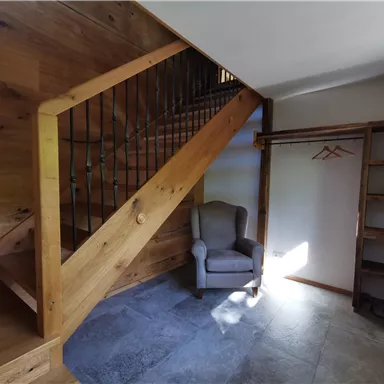 An inviting entrance area with a wooden staircase and a cozy armchair. There is a shelf and a coat rack on the wall.