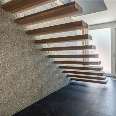 Eine moderne Treppe aus Holz und Beton führt in einen hellen Eingangsbereich. Die Wände sind schlicht und der Boden ist dunkel gefliest.