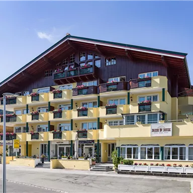 Ein modernes Hotelgebäude mit mehreren Etagen und Balkonen. Die Umgebung ist von grünen Hügeln umgeben und vermittelt eine einladende Atmosphäre.