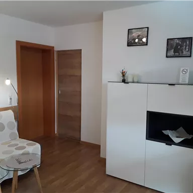 A bright living room with a beige sofa and a modern white cabinet. Some pictures hang on the wall, and the wooden floor gives the room a cozy atmosphere.