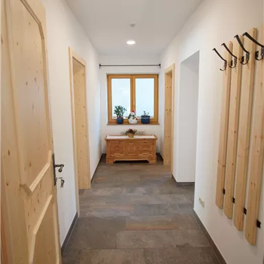 Ein heller Flur mit Holzdetails und einem Fenster. An der Wand befinden sich Garderobenhaken und ein Dekorationsstück auf einer Kommode.