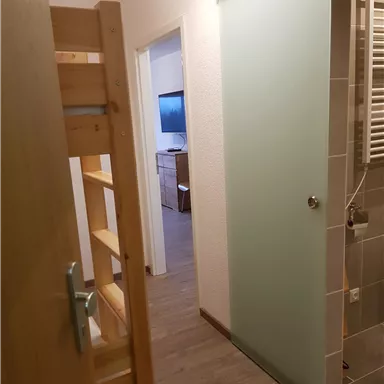 A cozy hallway with a shower cabin and a shelf. In the background, a room with a television is visible.