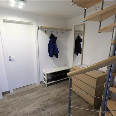 Ein heller Flur mit einer Treppe, einem Spiegel und einem Garderobenständer. Es gibt eine Sitzbank und einen geschlossenen Schrank an der Wand.