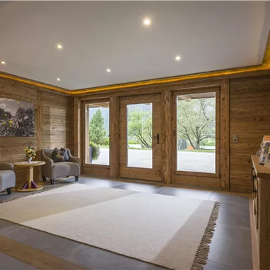 Ein einladender Eingangsbereich mit Holzwänden und modernen Möbeln. Große Fenster bieten einen Blick auf den Außenbereich.