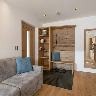 Ein heller Eingangsbereich mit einem gemütlichen Sofa und einer Holzablage. Der Raum hat eine moderne Einrichtung und einen großen Spiegel.