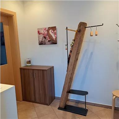 Ein moderner Eingangsbereich mit einem Holzregal und einer dekorativen Wand. Im Hintergrund hängt ein Bild, das eine herzliche Atmosphäre schafft.