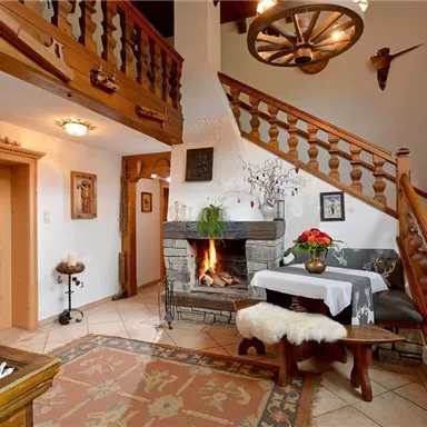A cozy living space with a wooden staircase and a fireplace. The decor is rustic, featuring a beautiful plant and decorative elements.