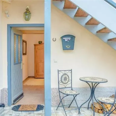 A cozy entrance area with a staircase, a small table, and two chairs. Next to the door is a stack of wood.