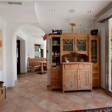 Ein einladender Raum mit einem Holzschrank und einem schönen Fliesenboden. An der Wand sind freundliche Gemälde zu sehen, die eine gemütliche Atmosphäre schaffen.