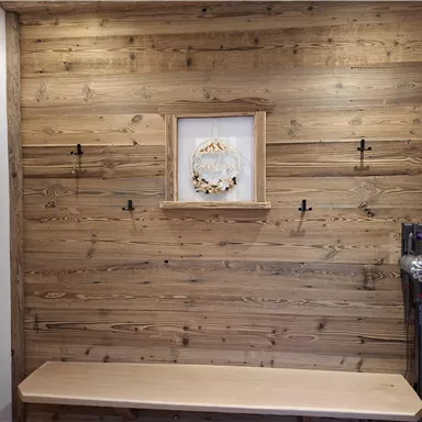 Eine helle Holzwand mit einer zentralen Wanddekoration und mehreren Haken. Darunter befindet sich eine einfache Holzbank.
Akkustaubsauger vorhanden