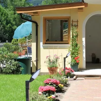 An inviting entrance area with a well-kept garden and colorful flowers. In the background, there is a blue sky and trees.