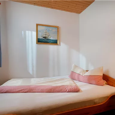 Ein gemütliches Schlafzimmer mit einem Einzelbett und einer maritimen Wandmalerei. Weiche Kissen und ein Fenster, das Licht hereinlässt, schaffen eine einladende Atmosphäre.