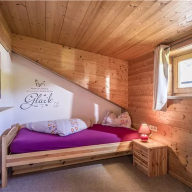 Ein gemütliches Zimmer mit Holzwänden und einem Einzelbett. Ein Fenster lässt natürliches Licht herein und es gibt eine dekorative Vase auf dem Tisch.