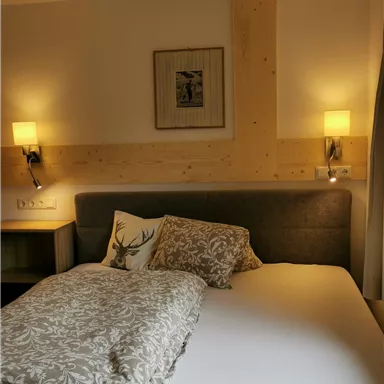 Ein gemütliches Schlafzimmer mit einem großen Bett, einer dekorativen Decke und sanftem Licht von den Lampen. An der Wand hängt ein Bild, und es gibt ein Möbelstück neben dem Bett.