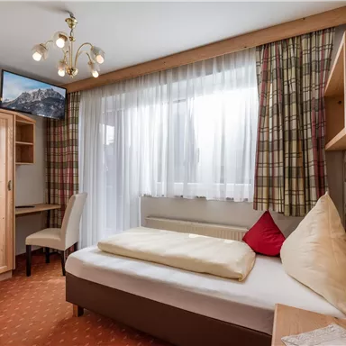 A cozy single room with bright light and modern furniture. The room contains a bed, a desk, and a television.