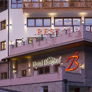 A modern hotel building with elegant architecture and warm lighting. The hotel sign "Berghof" is clearly visible and inviting.