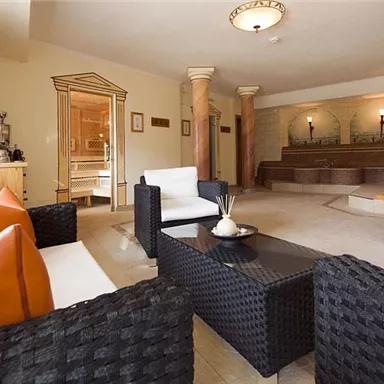 An elegant wellness area with comfortable black furniture and decorative cushions. In the background, a relaxing water basin is visible.