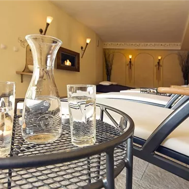 An elegant relaxation room with comfortable loungers and soft lighting. On a table, there are glasses and a carafe of water.